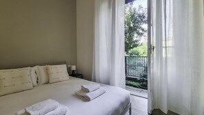 A bedroom with a bed, pillows, a nightstand, and a view of a balcony with greenery. - Italianway Easy - Ozieri 7 (Milan)