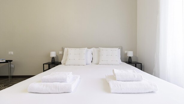 A hotel room with a large bed, two bedside tables with lamps, and towels on the bed. - Italianway Easy - Ozieri 7 (Milan)
