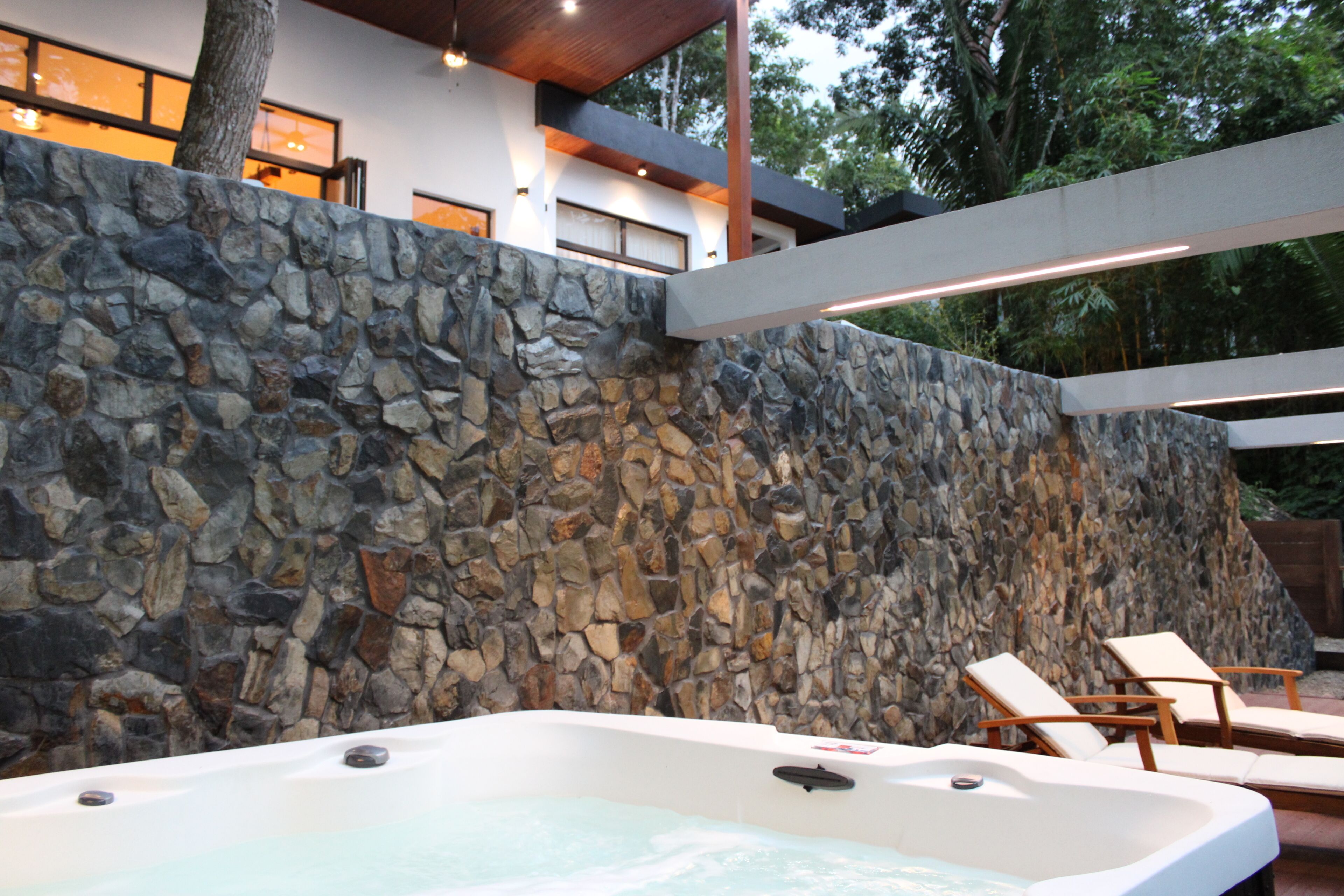 A stone wall, a hot tub, and lounge chairs.