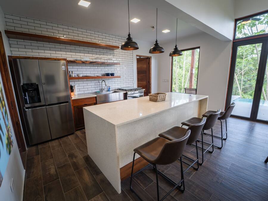 A modern kitchen with a large island, bar stools, and a view of the outdoors.