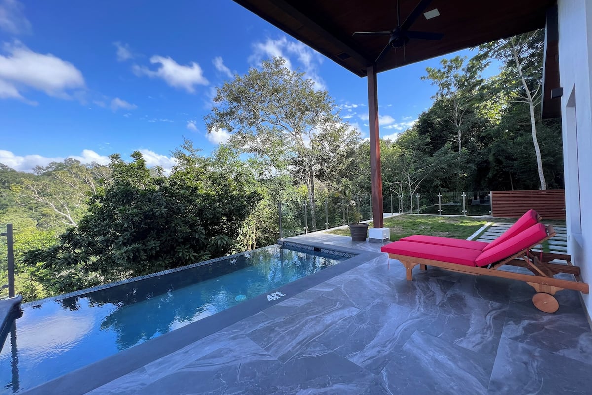 Un área de piscina exterior moderna con vistas despejadas del paisaje circundante, incluyendo árboles y una cadena montañosa distante.