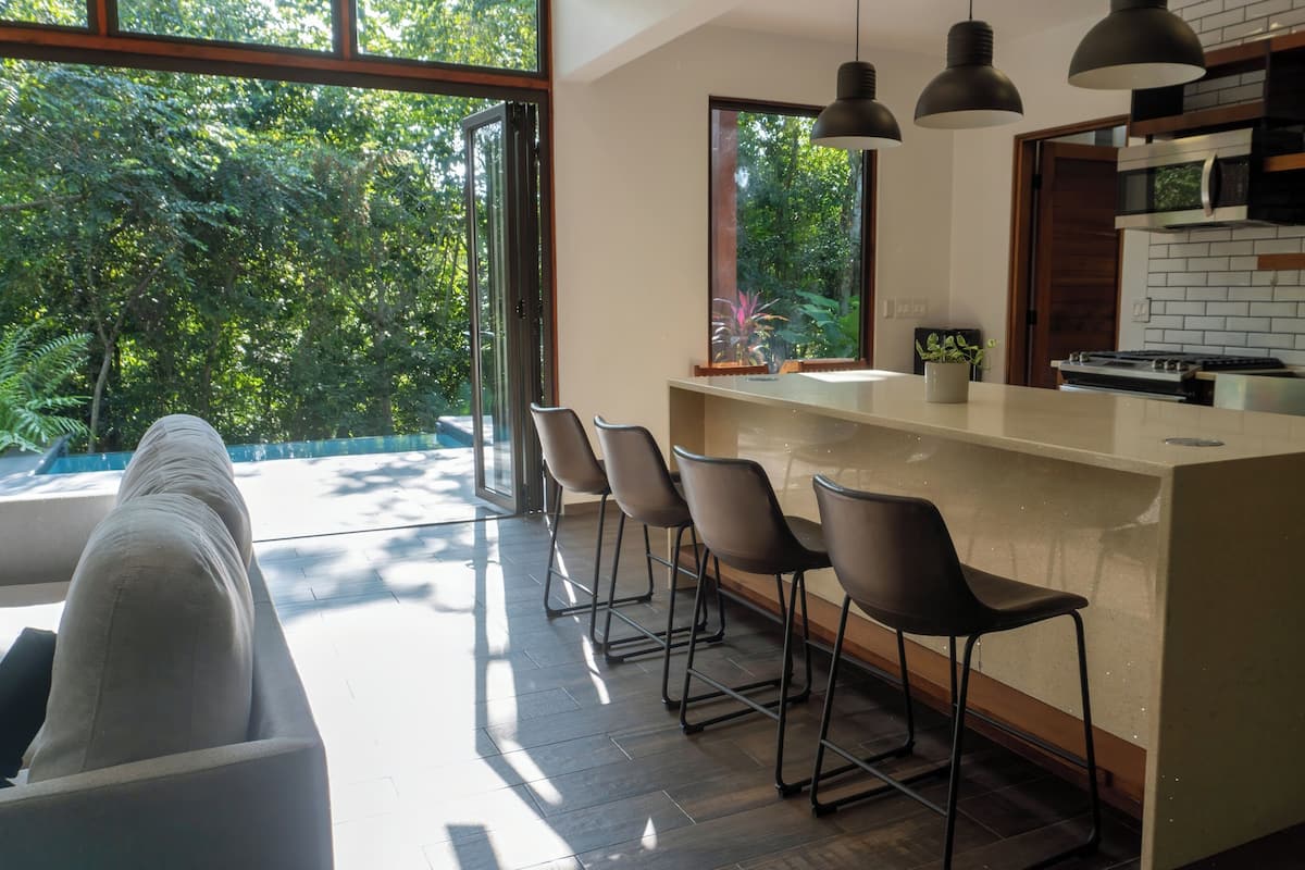 Una cocina moderna con una isla grande, taburetes de bar y vistas a vegetación exuberante.