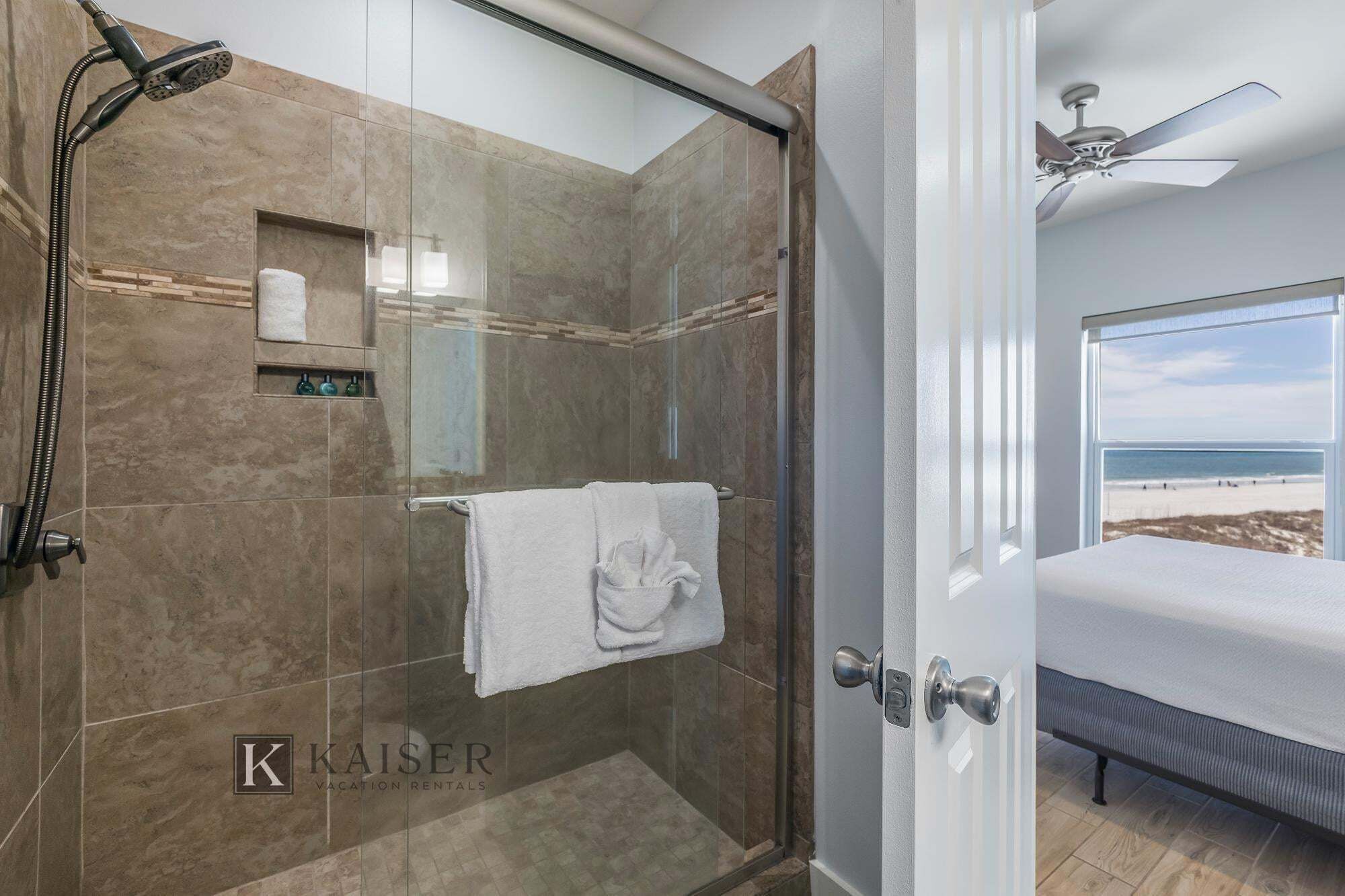 Une salle de bain moderne avec une douche à parois de verre, un porte-serviettes et une vue dégagée sur la plage par une fenêtre.
