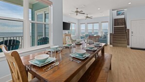 Una àmplia zona de dinar amb una llarga taula de fusta preparada per a sis, grans finestres que ofereixen vista a l'oceà i una escala que mena a un nivell superior.