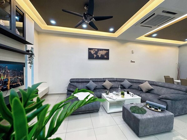 A modern living room with a grey sectional sofa, a white coffee table, and a ceiling fan. - JPP HOMESTAY (Johor Bahru)