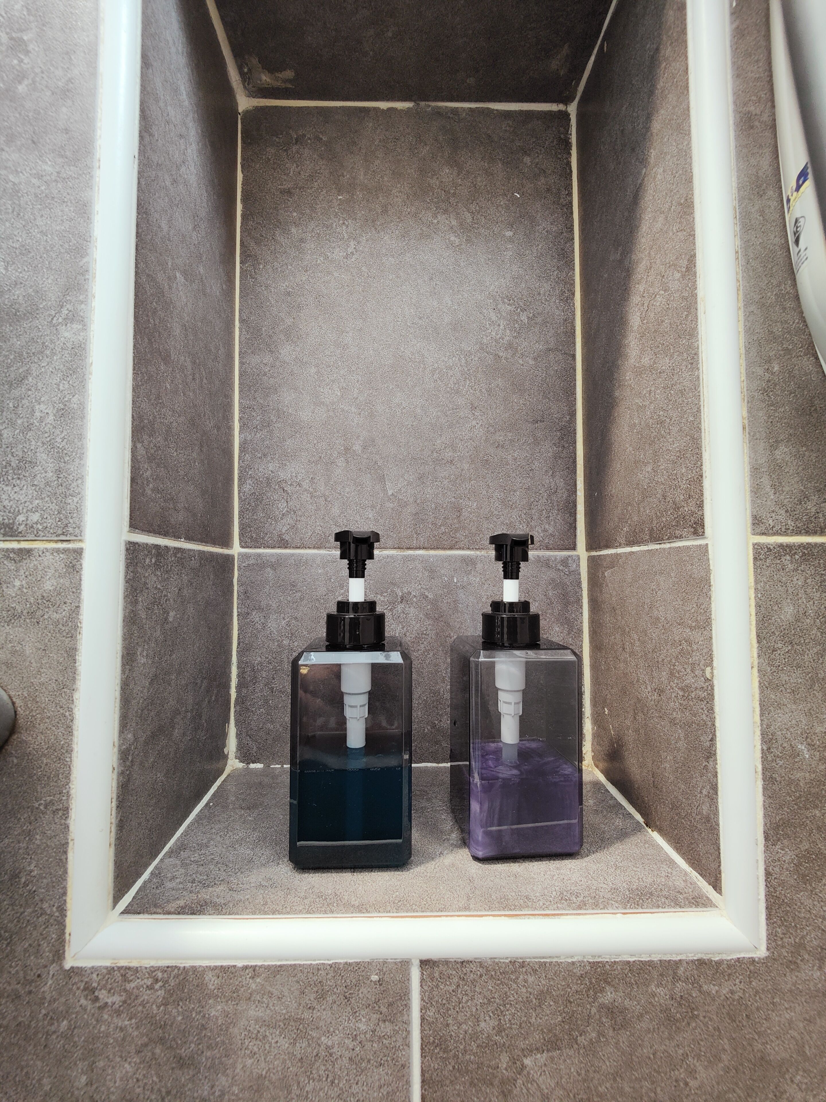 A shower area with two soap dispensers in a tiled enclosure.
