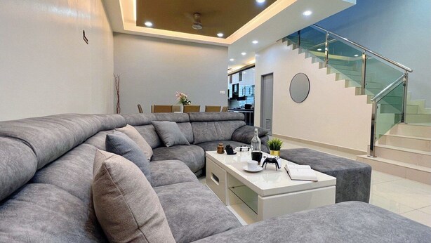 Un salon moderne avec un canapé d’angle gris, une table basse blanche et un escalier doté de rampes en verre.