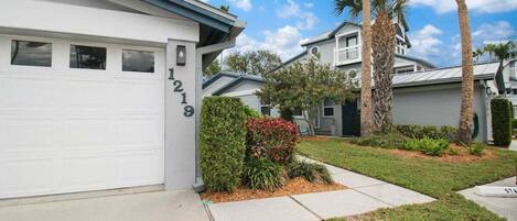 A residential building with a garage, numbered 1218, and a well-maintained lawn with palm trees.