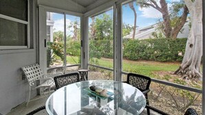 A conservatory with a glass table and chairs, large windows, and a view of a garden.