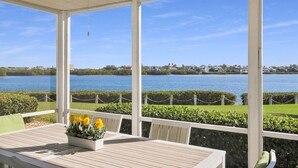 A covered outdoor area with a table and chairs, overlooking a body of water and a distant shoreline. - Gorgeous bay views from this ground floor Siesta Key Condo - GBB 1360 (Siesta Key)