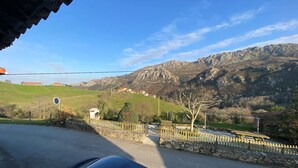 A rural road with a stone wall and wooden fence, leading to a mountainous landscape with houses in the background. - Casa El Marizal 2 Arriondas (Montealea)