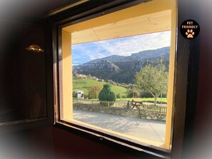 A window with a view of a rural landscape, including mountains, a stone wall, and a wooden fence.