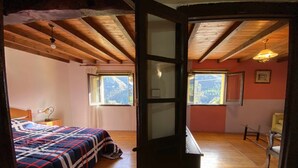 A bedroom with a bed, a desk, and a chair. There are two windows and a view of the outdoors. - Casa El Marizal 2 Arriondas (Montealea)