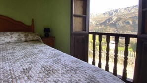 Un dormitorio con una cama, una mesita de noche y una ventana que ofrece vistas a las montañas.