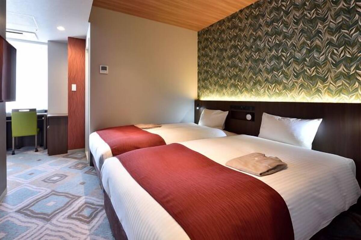 Habitación de hotel con dos camas, un escritorio y un papel tapiz estampado.