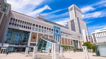 A modern building with a large glass facade, a prominent clock, and a spacious plaza with stone pillars.