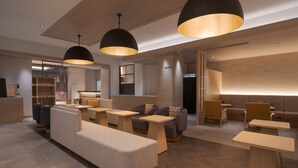 Een moderne hotellobby met zithoeken, houten tafels en hanglampen.