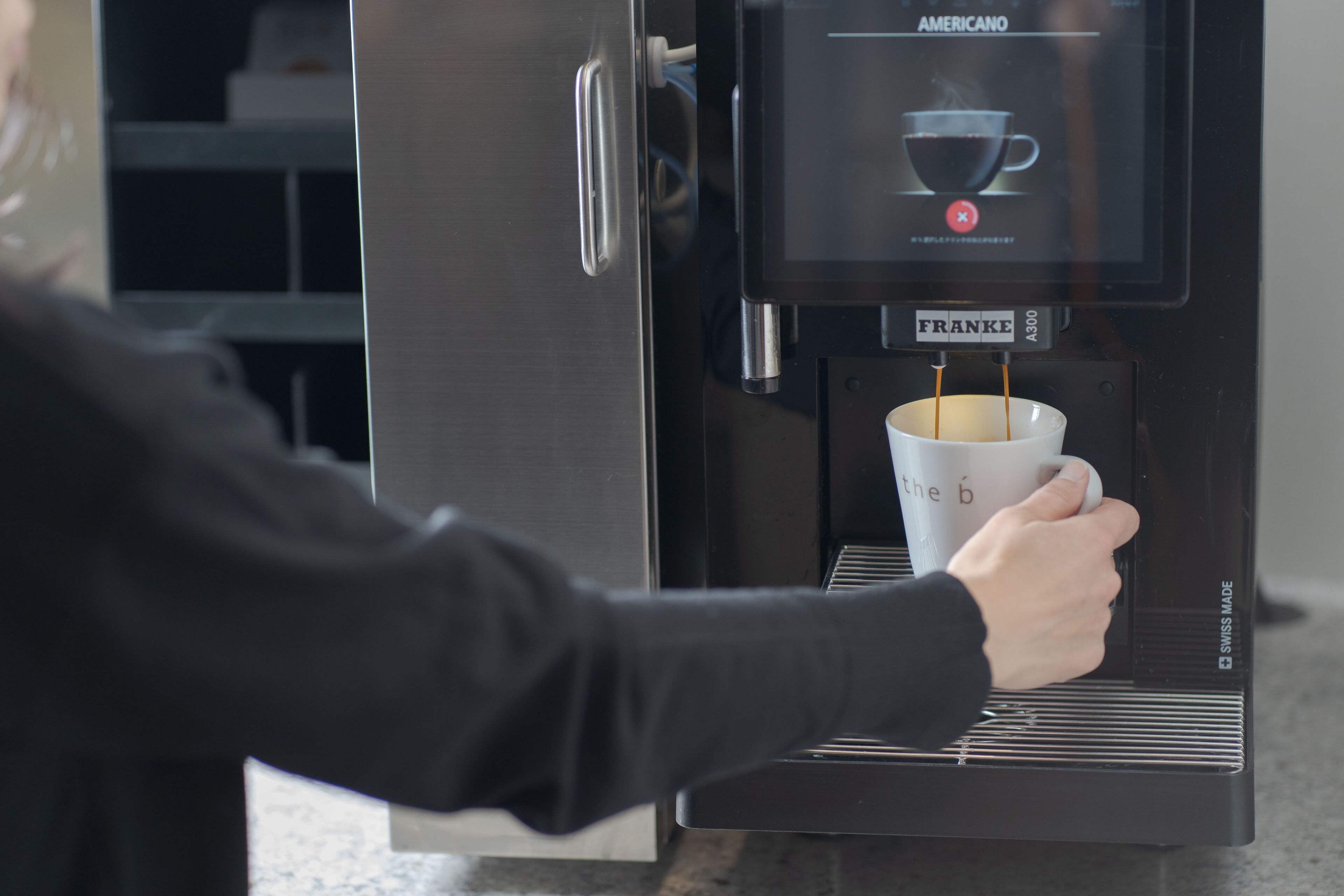 A person using a coffee machine with a digital display, dispensing coffee into a cup.