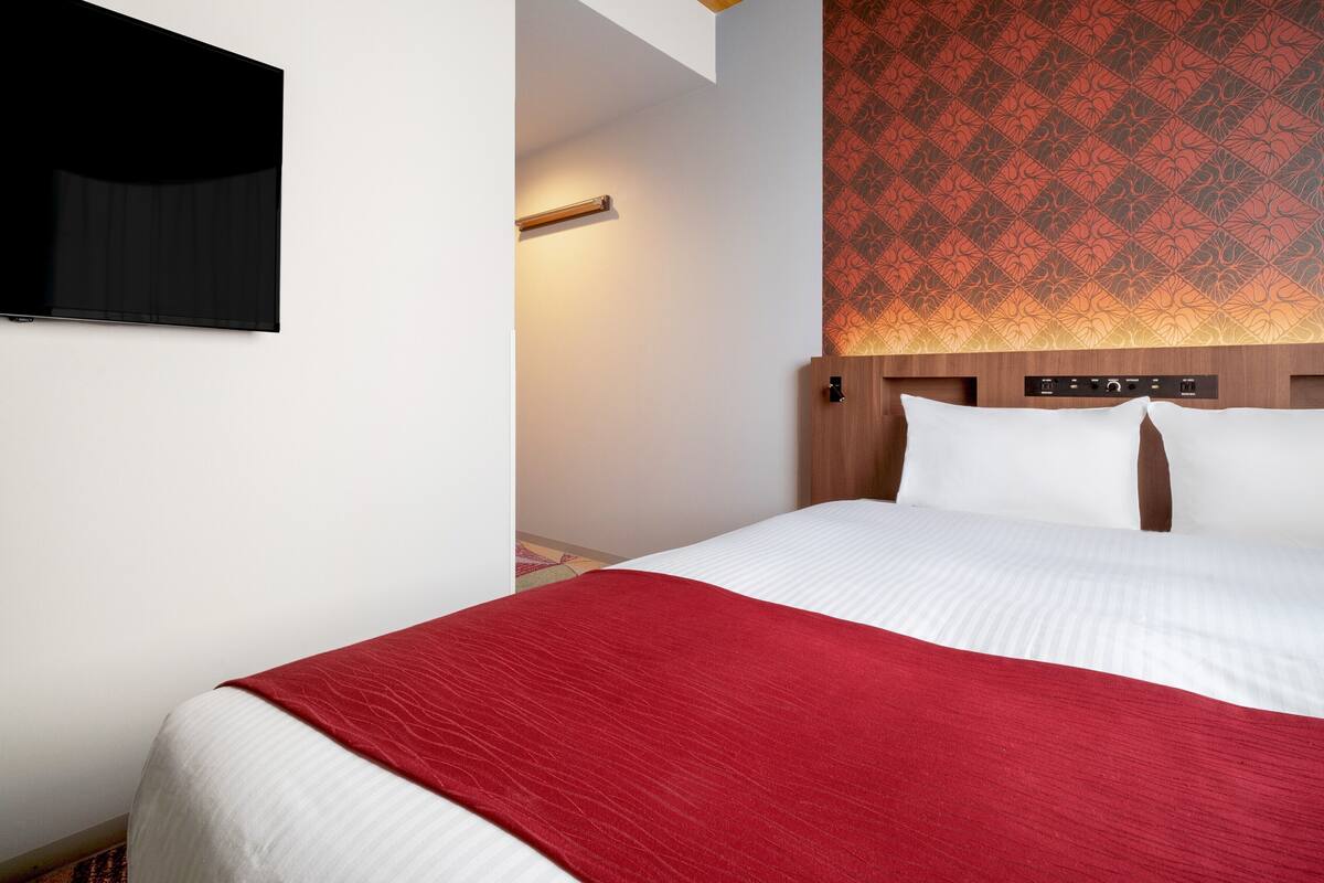 Habitación de hotel con cama, televisor montado en la pared y papel tapiz estampado.