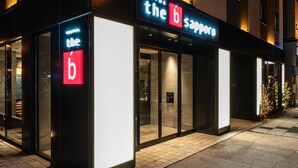 Een hotelentree met een opvallend 'b' logo, glazen deuren en een betegeld pad.