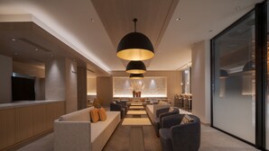 Een moderne hotellobby met een bank, stoelen, een bijzettafeltje en een groot raam.
