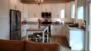 Una cocina moderna con armarios blancos, electrodomésticos de acero inoxidable, una araña y una zona de bar con taburetes.