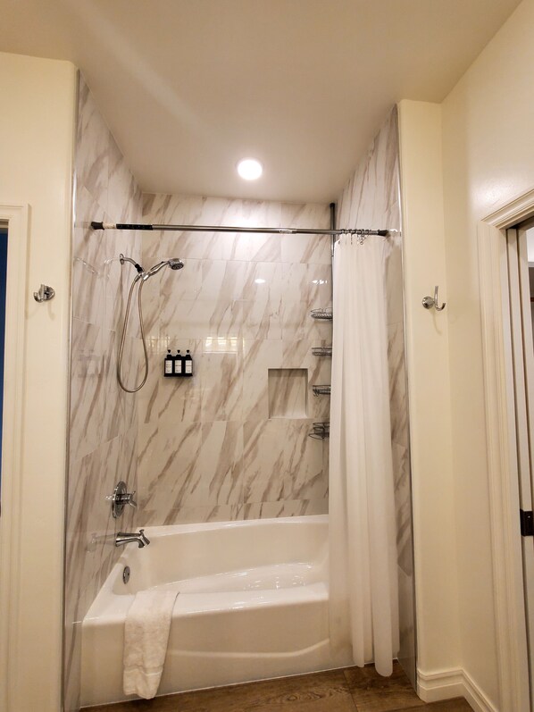 A modern bathroom with a glass-enclosed shower, a white bathtub, and marble walls.