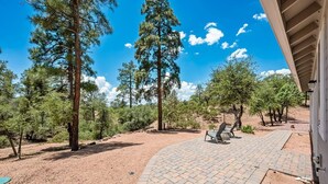 Un patio empedrado con mobiliario exterior, rodeado de árboles y un cielo despejado.