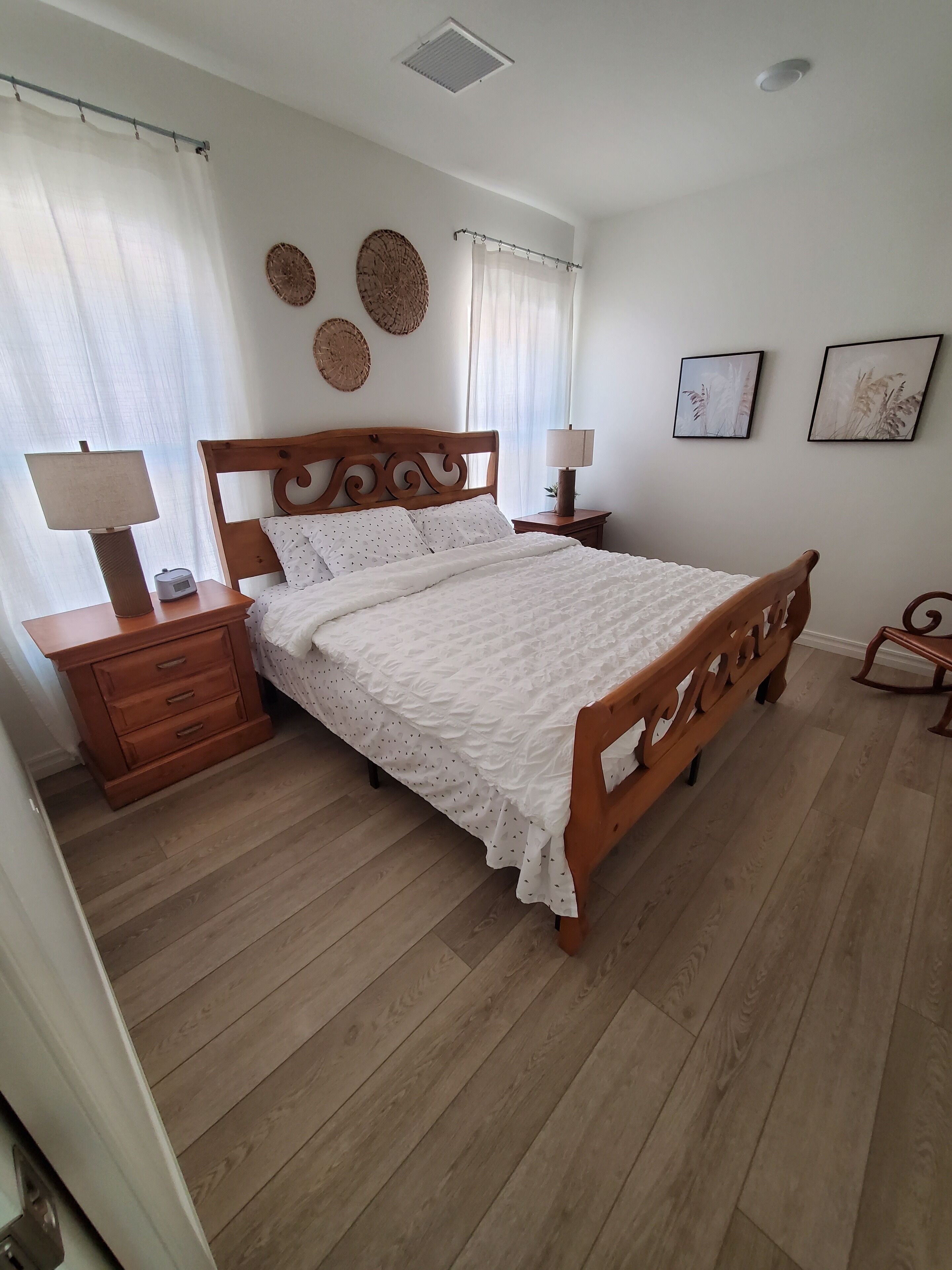 Una camera da letto con un letto in legno, un comodino con una lampada, una cassettiera e due lampade a parete.