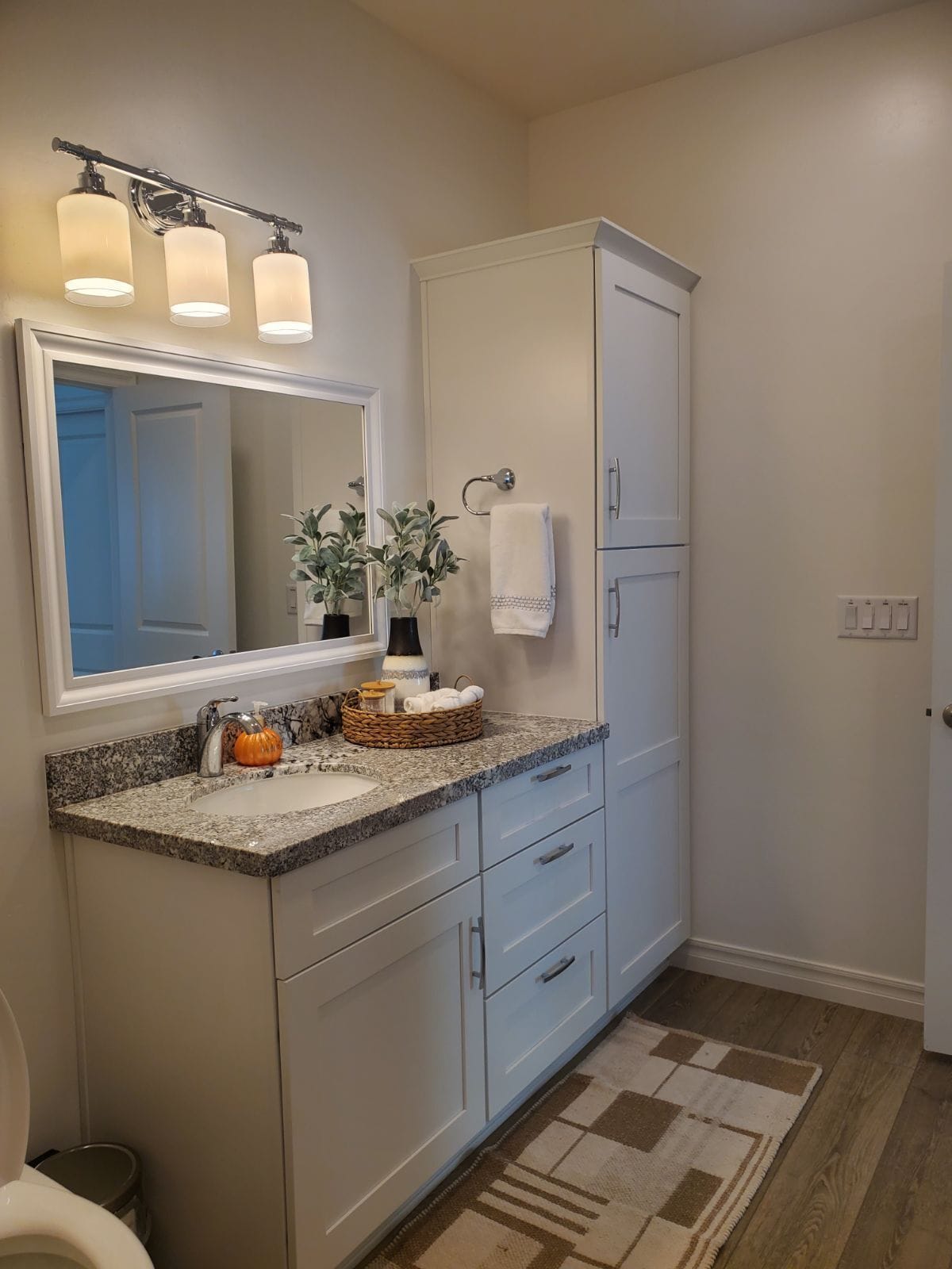 Un baño con encimera de granito, un espejo grande, toallero y suelo de madera.