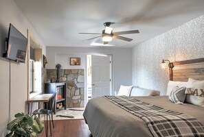 A bedroom with a bed, a desk, a television, a ceiling fan, and a stone fireplace.