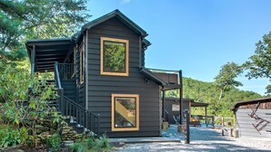 A two-story cabin with a covered porch and a stone wall.