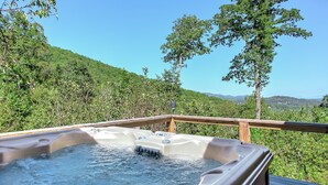 Un jacuzzi en una terraza de madera con vista a una ladera boscosa.