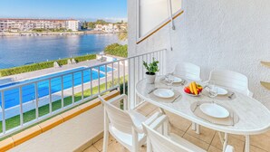 Ein Balkon mit Pool, weißen Stühlen, einem Tisch für zwei Personen und Blick auf einen Fluss und Gebäude.
