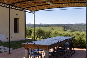 An outdoor patio with a table and chairs, a covered area with a view of a hilly landscape. - Villa Il Caggio - San Gimignano ,Tuscany (San Gimignano)