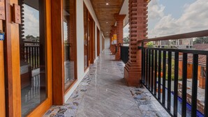 A corridor with wooden doors and windows, a tiled floor, and a balcony with a black railing.