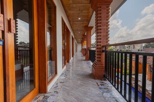 A corridor with wooden doors and windows, a tiled floor, and a balcony with a black railing.