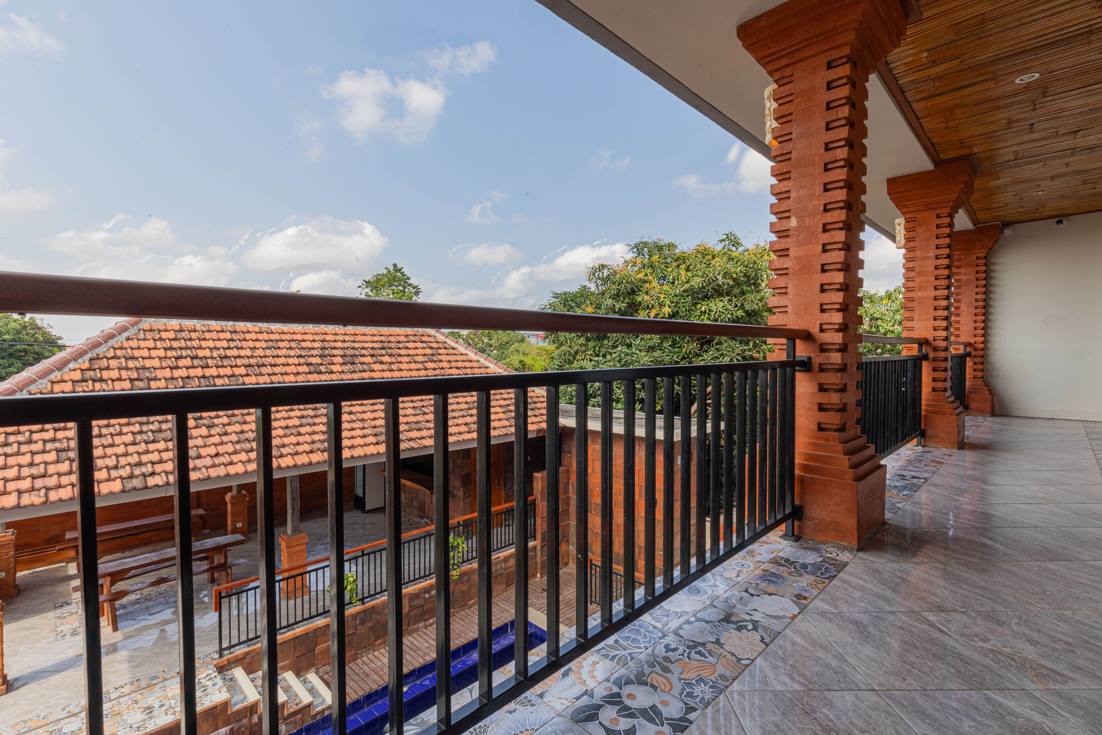 A balcony with a tiled floor, a wooden bench, and a view of a building with a tiled roof.