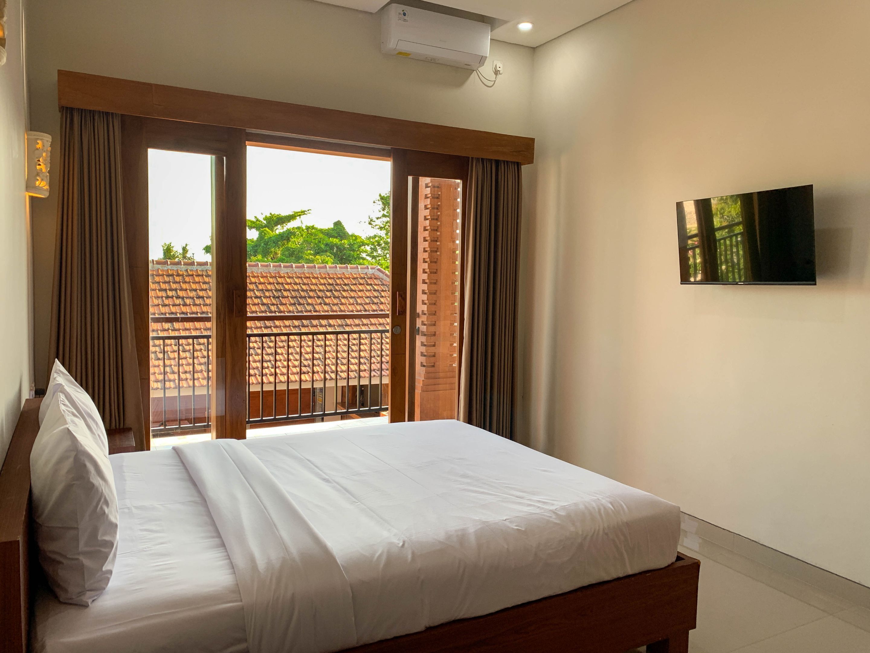 Habitación de hotel con cama, televisión en la pared y vistas a un edificio con tejado de tejas.