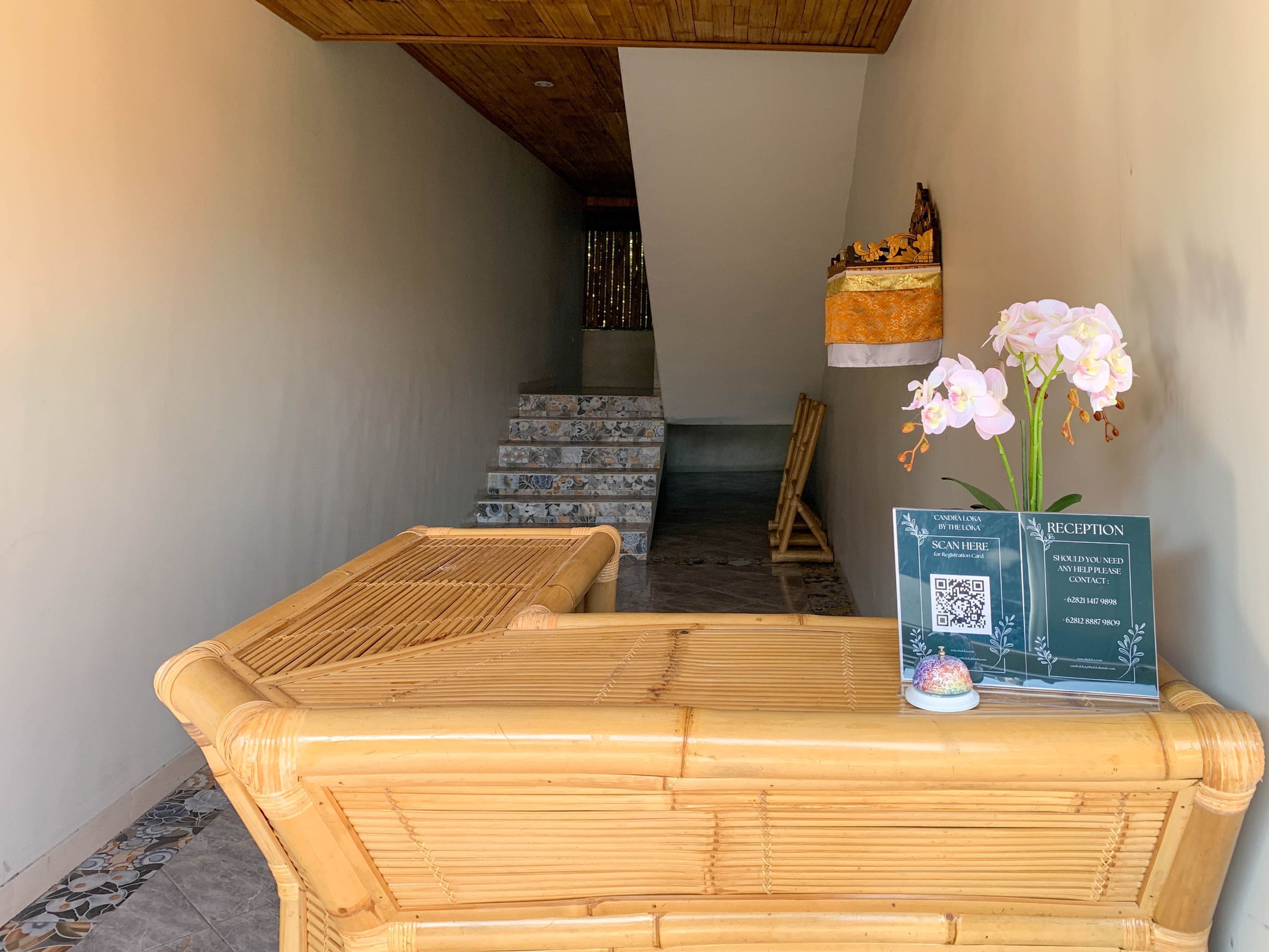 Un área de recepción con mostrador, un código QR para registrarse y un jarrón decorativo con flores.