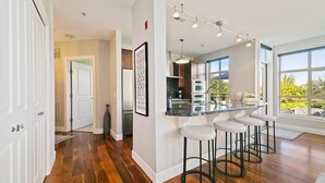 A modern kitchen with a central island, bar stools, and a large window providing a view of the outdoors.