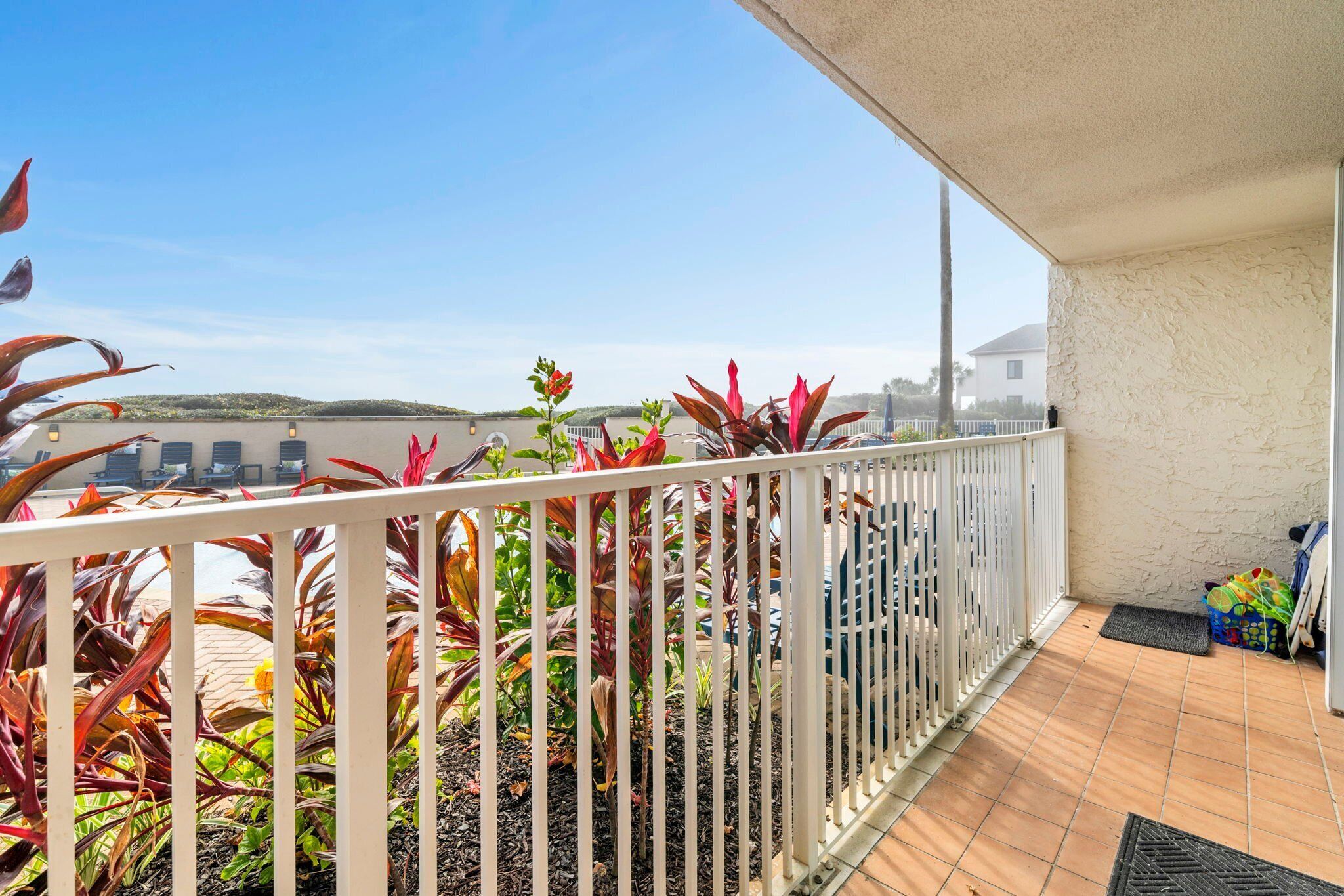 A balcony with a white railing, potted plants, and a view of the surrounding area.