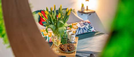 Ein gemütliches Zimmer mit einem Bett, bunten Kissen, einer Tablett mit Gebäck, Gläsern und einer Blumenvase.