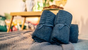 A pair of folded towels on a textured surface, possibly a bed or couch, with a blurred background suggesting a cozy indoor setting. - Cute studio for a couple or young family located near parks (Rīga)