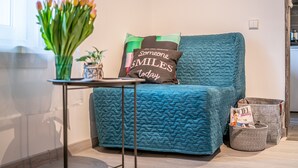 A teal upholstered sofa with a quilted pattern, a vase with tulips, and a cushion with the text "Someone SMILES today". - Cute studio for a couple or young family located near parks (Rīga)