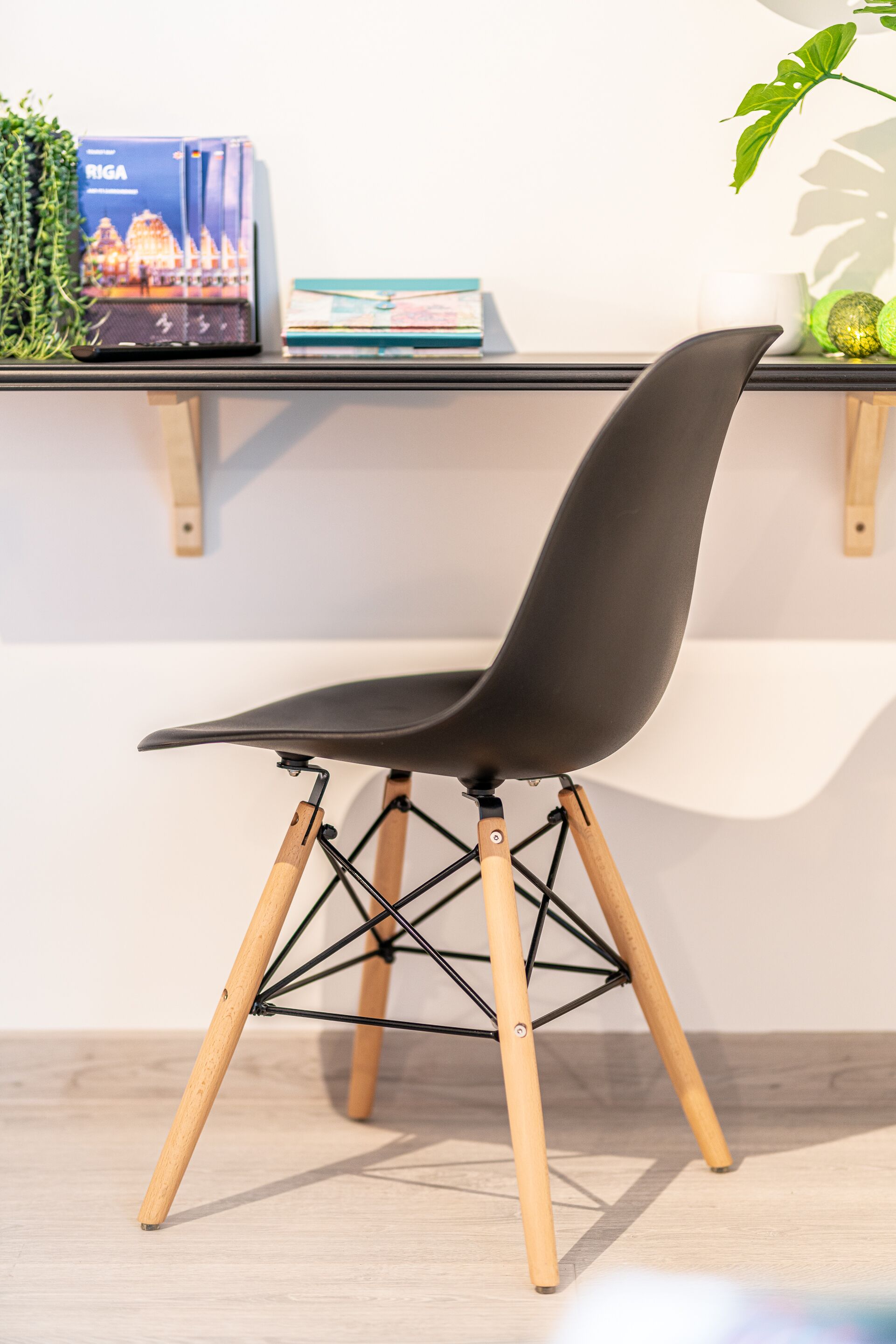 Une chaise moderne avec un siège noir et des pieds en bois, placée devant une étagère contenant des livres et une plante.