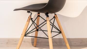 Une chaise moderne avec un siège noir et des pieds en bois, placée devant une étagère contenant des livres et une plante.