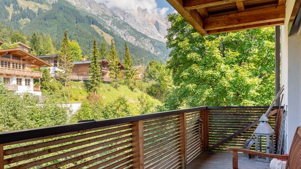 Ein Holzbalkon mit Blick auf eine gebirgige Landschaft, einschließlich Häusern und Bäumen.