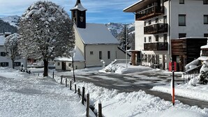 Eine verschneite Straße mit einer Kirche, einem Baum und Gebäuden mit Balkonen.
