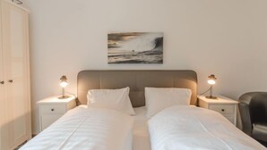 A hotel room with two beds, a headboard, bedside lamps, a painting of a wave, and a door. - Apartment Smilla by Interhome (Bad Gastein)